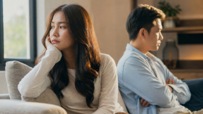 Pasangan Indonesia duduk berjarak di sofa ruang tamu, saling berbicara dengan tenang tentang trust issue dan kepercayaan yang hilang